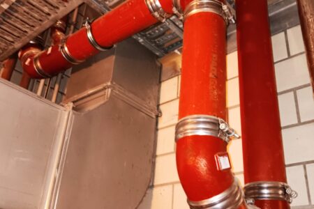 Neu installierte rote Gussrohre einer Abwasseranlage mit Rohrbögen und Edelstahlverbindern.