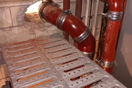 Neu montierte rote Gussrohre für die Abwasserinstallation mit Rohrschellen und Wanddurchführungen.