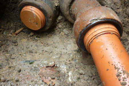 Orange Kunststoff-Abwasserrohre, die im Erdreich an ältere Abwasserrohre angeschlossen sind.