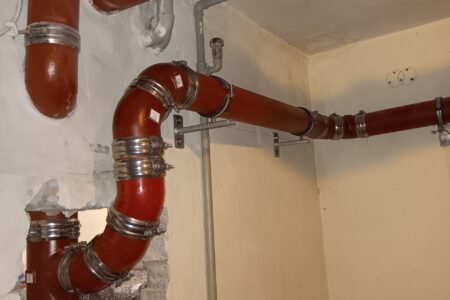 Neu verlegte rote Abwasserrohre aus Guss mit Rohrschellen und Bögen an Wand und Decke eines Kellerraums.