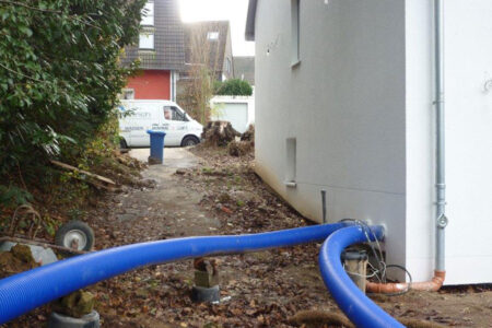Blaue Schläuche für Sanierungsarbeiten an der Abwasserleitung führen über das Grundstück zu einem Wohnhaus.