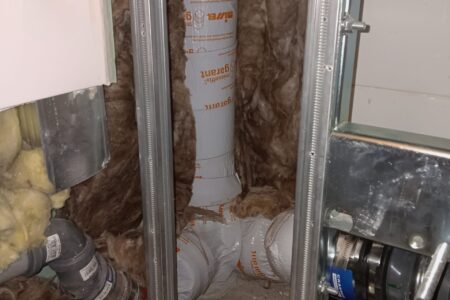 Gedämmte Abwasserleitung innerhalb einer geöffneten Vorwandkonstruktion mit Metallständerwerk und Mineralwolldämmung.