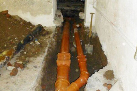 Orange Abwasserrohre mit Abzweig in einem geöffneten Kellerboden während der Neuverlegung.