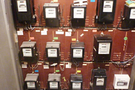 Alte Elektroverteilung mit mehreren mechanischen Stromzählern und sichtbarer Verkabelung.