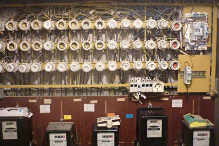 Alte elektrische Verteilung mit zahlreichen Schraubsicherungen, Stromzählern und umfangreicher Verkabelung.