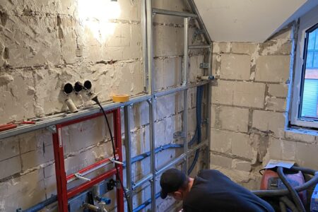 Handwerker montiert bei einer Badsanierung eine Vorwandinstallation mit Metallständerwerk und Sanitärleitungen.