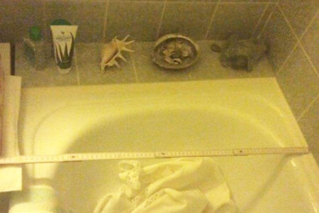 Eine eingebaute Badewanne wird mit einem Zollstock ausgemessen, um die Maße für die geplante Badsanierung zu bestimmen.