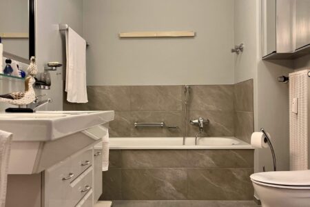 Helles Badezimmer mit Badewanne, Waschtisch, Toilette und grauen Fliesen.