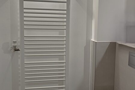 Weißer Handtuchheizkörper mit Thermostat an der Wand eines modern gestalteten Badezimmers