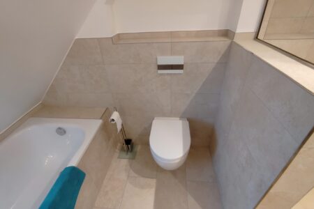 Modern saniertes Dachgeschossbad mit Badewanne, Wand-WC und hellen großformatigen Fliesen.
