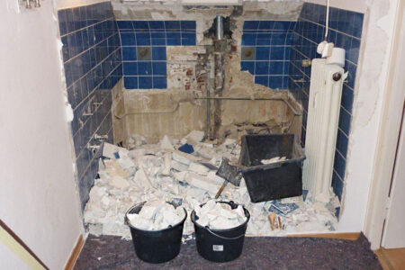 Entkerntes Badezimmer während der Badsanierung mit entfernten Sanitärobjekten, abgeschlagenen Fliesen und Bauschutt.