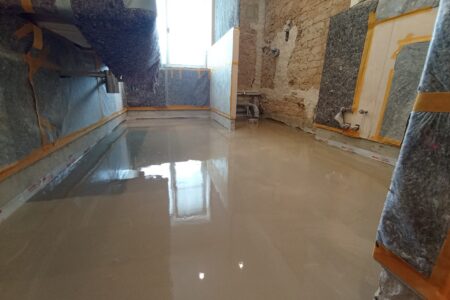 Badezimmer während der Sanierung mit frisch eingebrachtem Estrich, freigelegtem Mauerwerk und geschützten Installationen.