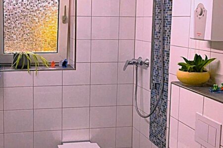 Geflieste Dusche mit Klappsitz, Haltegriff, Handbrause und bodennahem Duschbereich