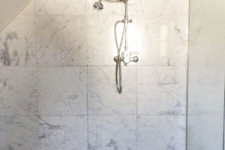 Begehbare Dusche mit großer Regendusche, Glasabtrennung und hellen Fliesen in Marmoroptik.