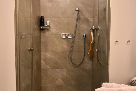 Moderne bodengleiche Dusche mit grauen Fliesen, Glasabtrennung, Kopfbrause und Handbrause.