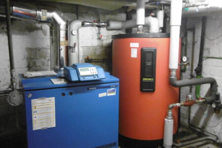 Heizungsraum mit blauem Buderus Heizkessel, rotem Fröling Warmwasserspeicher und angeschlossenen Rohrleitungen.