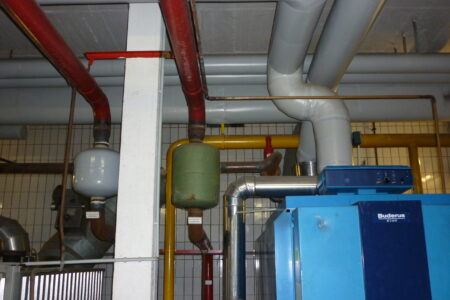 Buderus Heizungsanlage mit Rohrleitungen, Ausdehnungsgefäßen und Abgasführung in einem älteren Heizraum.