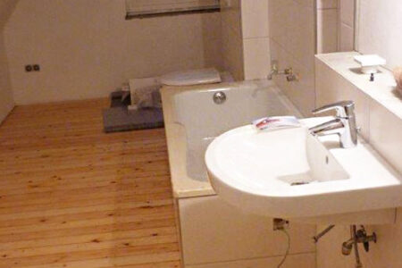 Renoviertes Badezimmer im Dachgeschoss mit Badewanne, Waschbecken, gefliester Wand und Holzdielenboden.