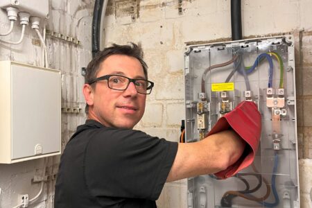 Elektriker bei Arbeiten an einer geöffneten Elektroverteilung mit Starkstromleitungen und elektrischen Anschlüssen