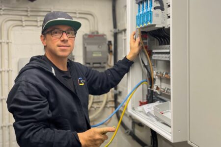 Elektriker bei Installationsarbeiten an einem geöffneten Schaltschrank mit elektrischen Leitungen und Sicherungskomponenten.