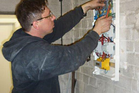 Fachhandwerker arbeitet an der Elektroinstallation eines geöffneten Sicherungskastens in einem Bestandsgebäude.