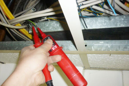 Spannungsprüfung mit einem zweipoligen Spannungsprüfer an elektrischen Leitungen in einer geöffneten Decke.
