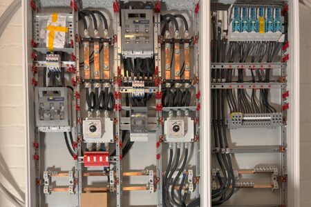 Geöffneter Schaltschrank mit Stromverteilung, Sicherungen, Kupferschienen und elektrischen Leitungen.