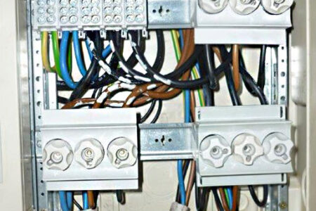Geöffnete Elektroverteilung mit Sicherungselementen, Anschlussklemmen und farblich gekennzeichneten elektrischen Leitungen.