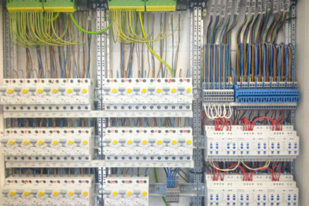 Geöffnete Elektroverteilung mit zahlreichen Sicherungen, Anschlussklemmen und übersichtlich verlegten elektrischen Leitungen.