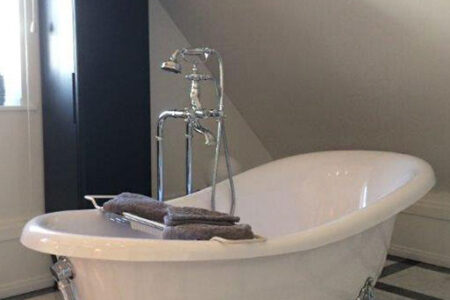 Freistehende Badewanne mit Füßen und klassischer Standarmatur in einem hellen Badezimmer.