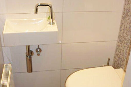 Modernes Gäste-WC mit kleinem Waschtisch, Wand-WC, Heizkörper und hellen Wandfliesen.