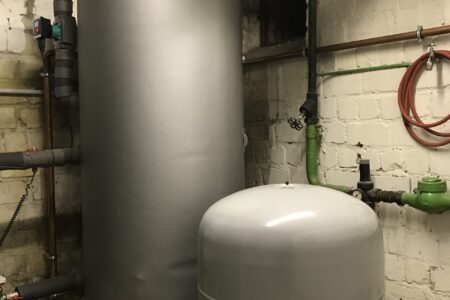 Großer Pufferspeicher mit Ausdehnungsgefäß und gedämmten Rohrleitungen in einem Heizungsraum.