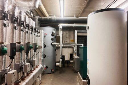 Technikraum mit großen Pufferspeichern, gedämmten Rohrleitungen, Umwälzpumpen und Komponenten der Heizungsanlage.