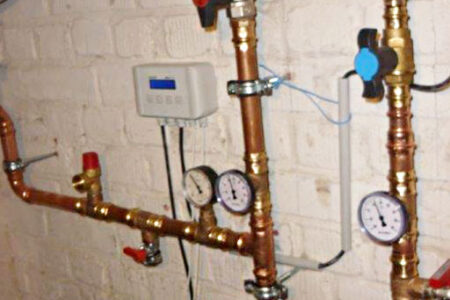 Heizungsinstallation mit Kupferrohren, Umwälzpumpen, Manometern und Regeltechnik an einer Kellerwand.