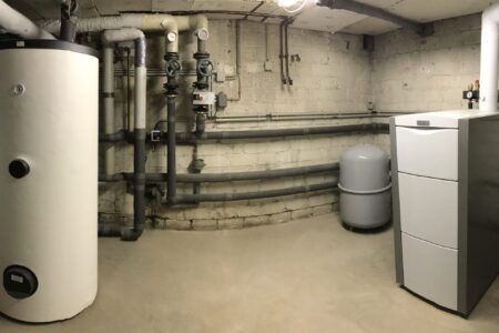Heizungsraum mit großem Warmwasserspeicher, modernem Heizkessel, Ausdehnungsgefäß und gedämmten Rohrleitungen.