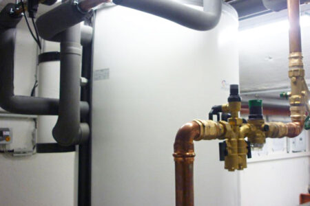 Warmwasserspeicher einer Heizungsanlage mit gedämmten Leitungen, Kupferrohren und Armaturen im Heizungsraum.