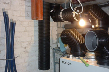 Lüftungsanlage von Maico mit mehreren schwarzen flexiblen Luftkanälen während der Installation im Keller.