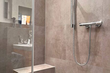 Moderne bodengleiche Dusche mit Glasabtrennung, großformatigen Fliesen, Handbrause und gefliester Sitzbank