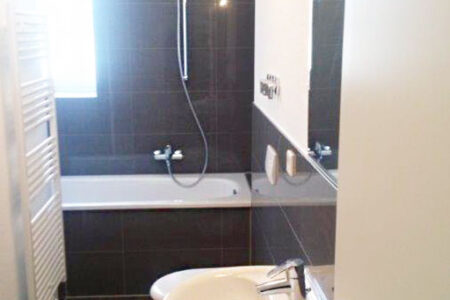 Modernes Badezimmer mit Badewanne, Waschtisch, Handtuchheizkörper und dunklen Wand- und Bodenfliesen.