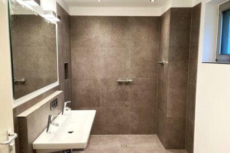 Modernes Badezimmer mit bodengleicher Dusche, großformatigen Fliesen und Doppelwaschbecken.
