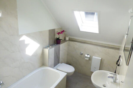 Modernisiertes Badezimmer unter einer Dachschräge mit Badewanne, Wand-WC, Waschbecken und Dachfenster.