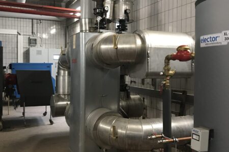 Modernisierte Heizungsanlage in einem großen Heizraum mit gedämmten Rohrleitungen, Armaturen und Wasseraufbereitung.