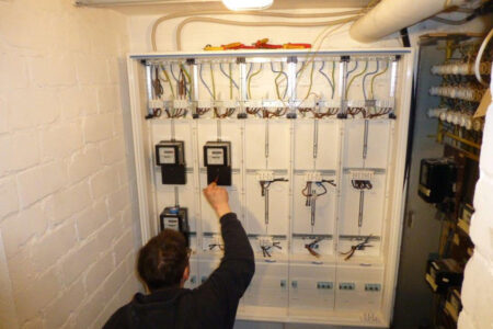Fachhandwerker bei Arbeiten an einer modernisierten Elektroverteilung mit mehreren Stromzählerplätzen.