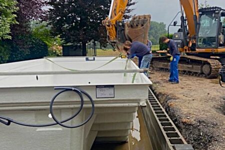 Handwerker setzen mit Unterstützung eines Baggers einen großen Fertigpool in die vorbereitete Baugrube ein.