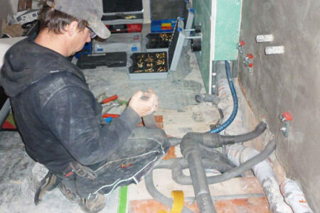 Fachhandwerker montiert Rohrleitungen und Anschlüsse während einer Sanitärinstallation in einem Gebäude.