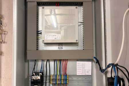 Geöffneter Schaltschrank mit Steuerungseinheit, Anschlussklemmen und farblich gekennzeichneten elektrischen Leitungen.