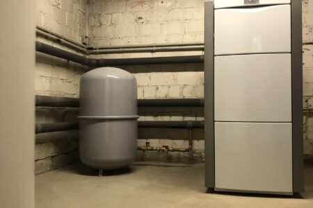 Moderne Vaillant Heizungsanlage mit grauem Ausdehnungsgefäß und gedämmten Rohrleitungen in einem Heizungsraum.