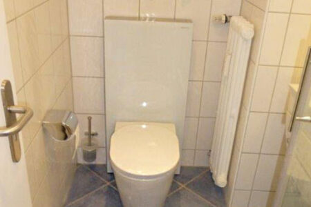 Fertig installiertes Wand-WC mit verkleideter Vorwand, Heizkörper und gefliesten Wänden in einem kleinen Badezimmer.