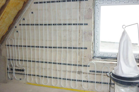 An der Innenwand eines Dachgeschosses verlegte Heizrohre einer Wandheizung vor dem Verputzen.