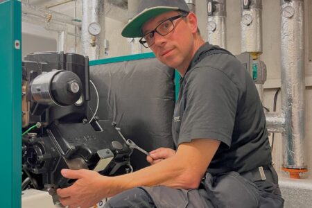 Fachhandwerker bei Wartungsarbeiten an einer Heizungsanlage in einem Technikraum mit gedämmten Rohrleitungen.